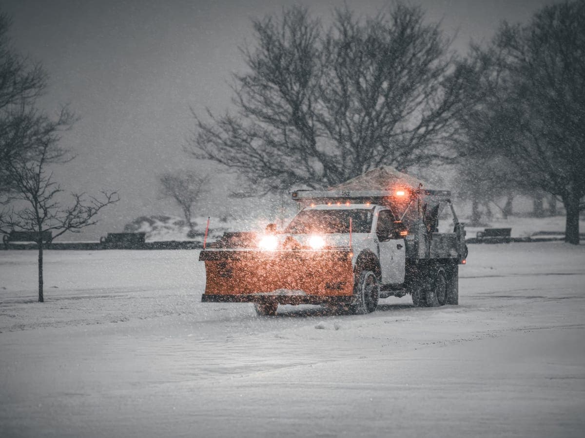 Un camión quitanieves con una pala frontal despejando nieve de una zona pavimentada abierta durante una fuerte nevada.