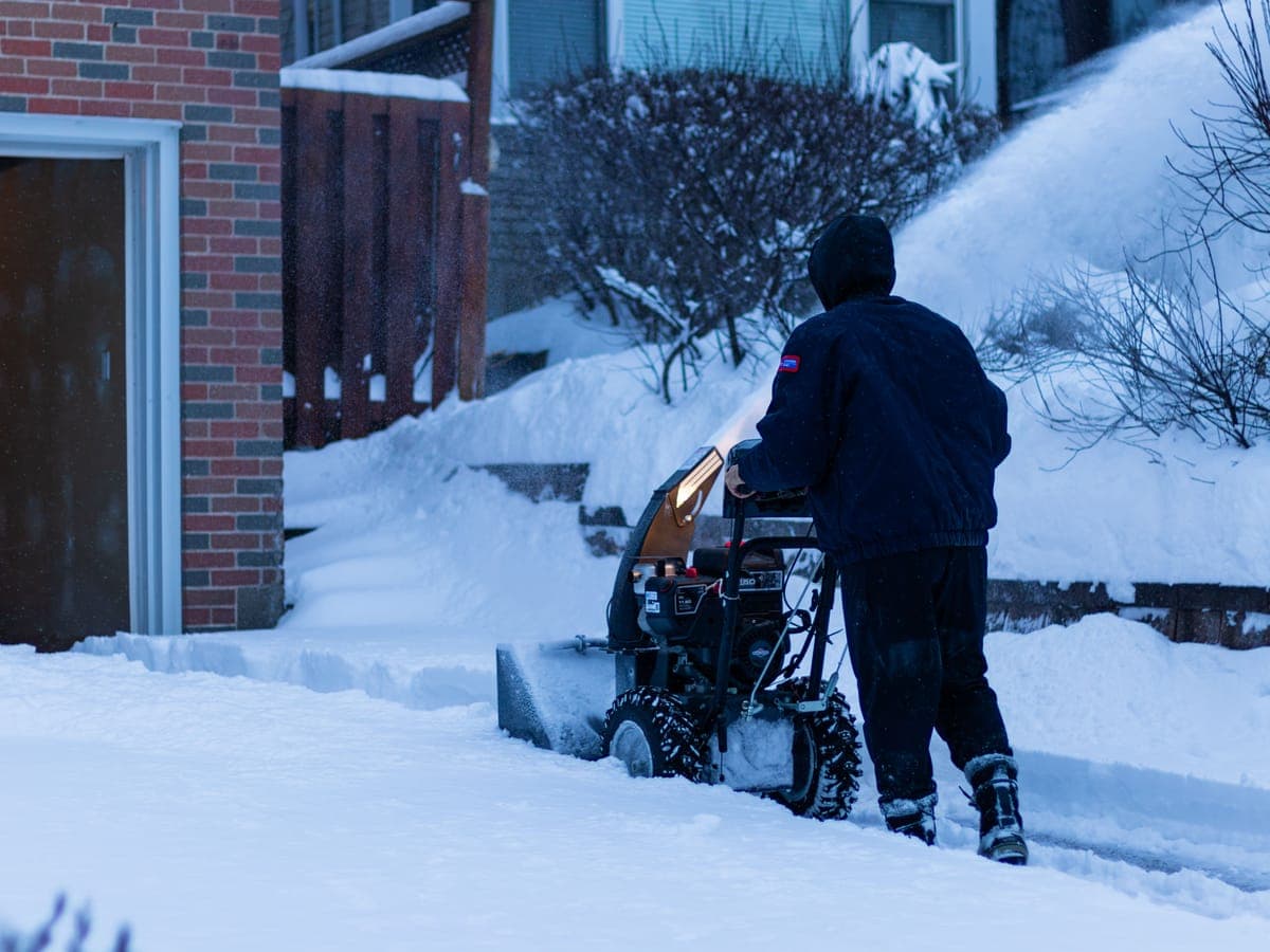 Una persona operando una máquina quitanieves de dos etapas para despejar nieve profunda de la entrada de una casa.