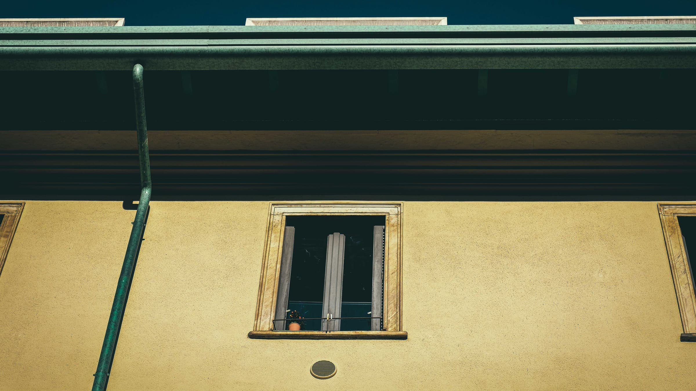 Green-painted metal rain gutter and downspout running along the eave and down the wall of a residential building.