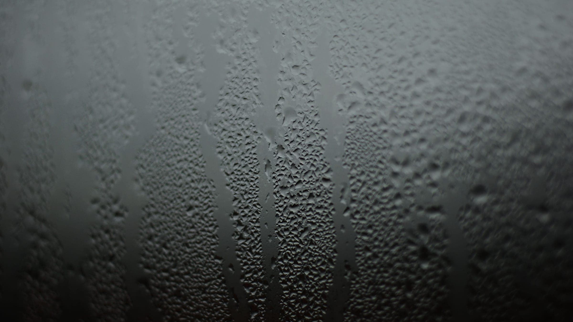 Heavy condensation and running water droplets covering the interior surface of a window pane.
