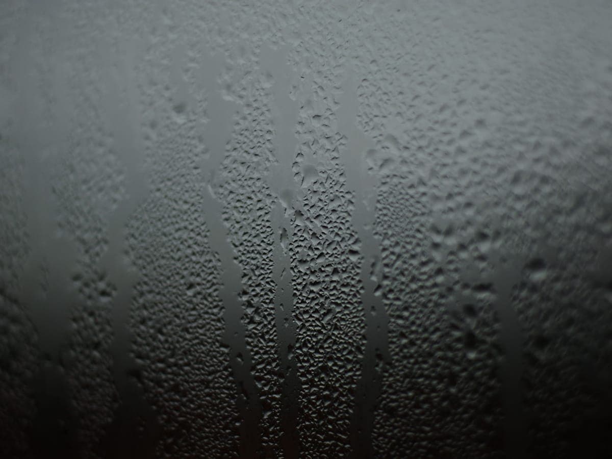 Condensación intensa y gotas de agua escurriendo que cubren la superficie interior del cristal de una ventana.