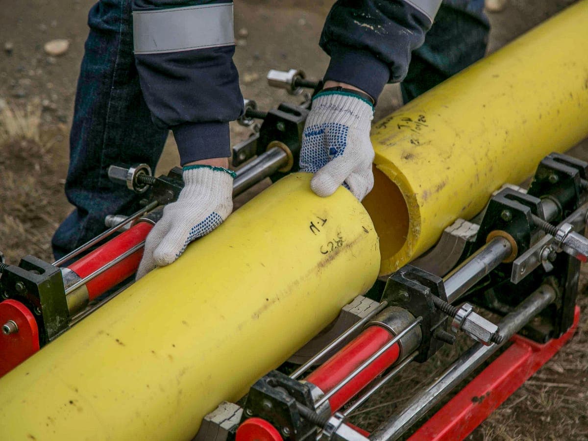 A gloved worker aligning a length of yellow polyethylene pipe clamped in a hydraulic butt-fusion machine for joining.