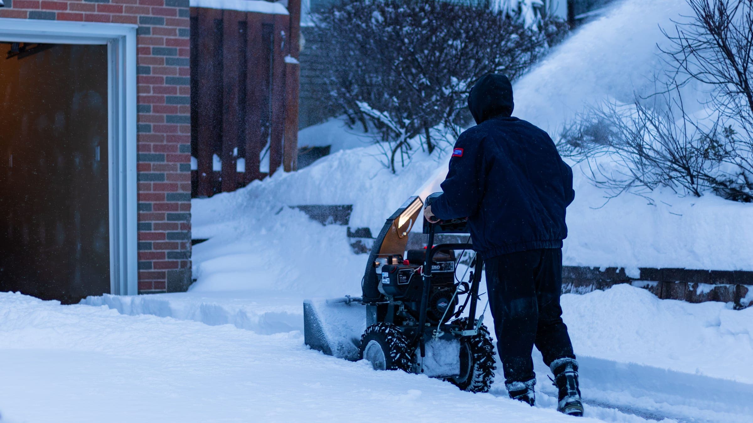 Una persona operando una máquina quitanieves de dos etapas para despejar nieve profunda de la entrada de una casa.