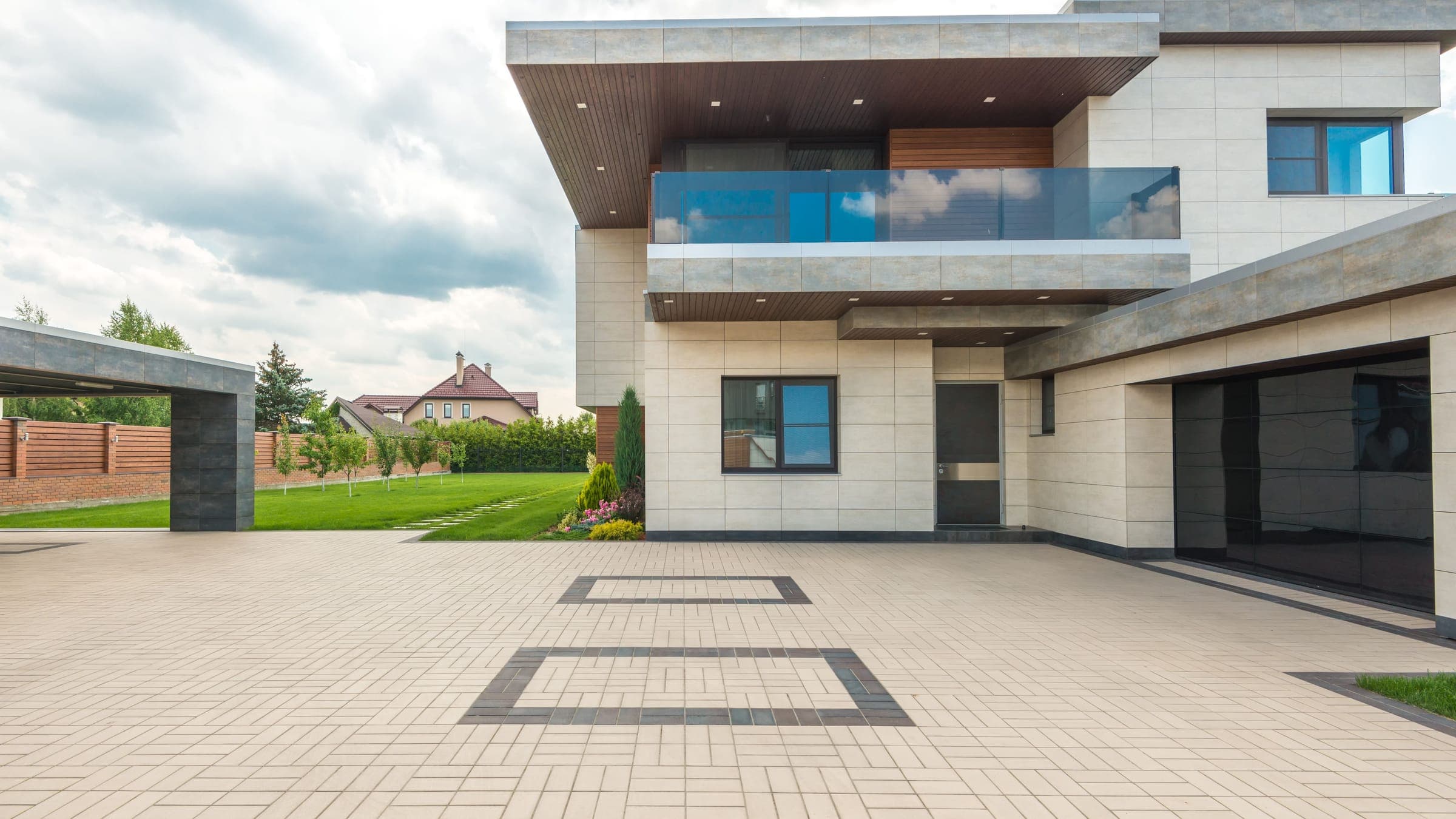 A wide interlocking-paver driveway with dark border insets leading up to the garage and entrance of a modern two-story home.