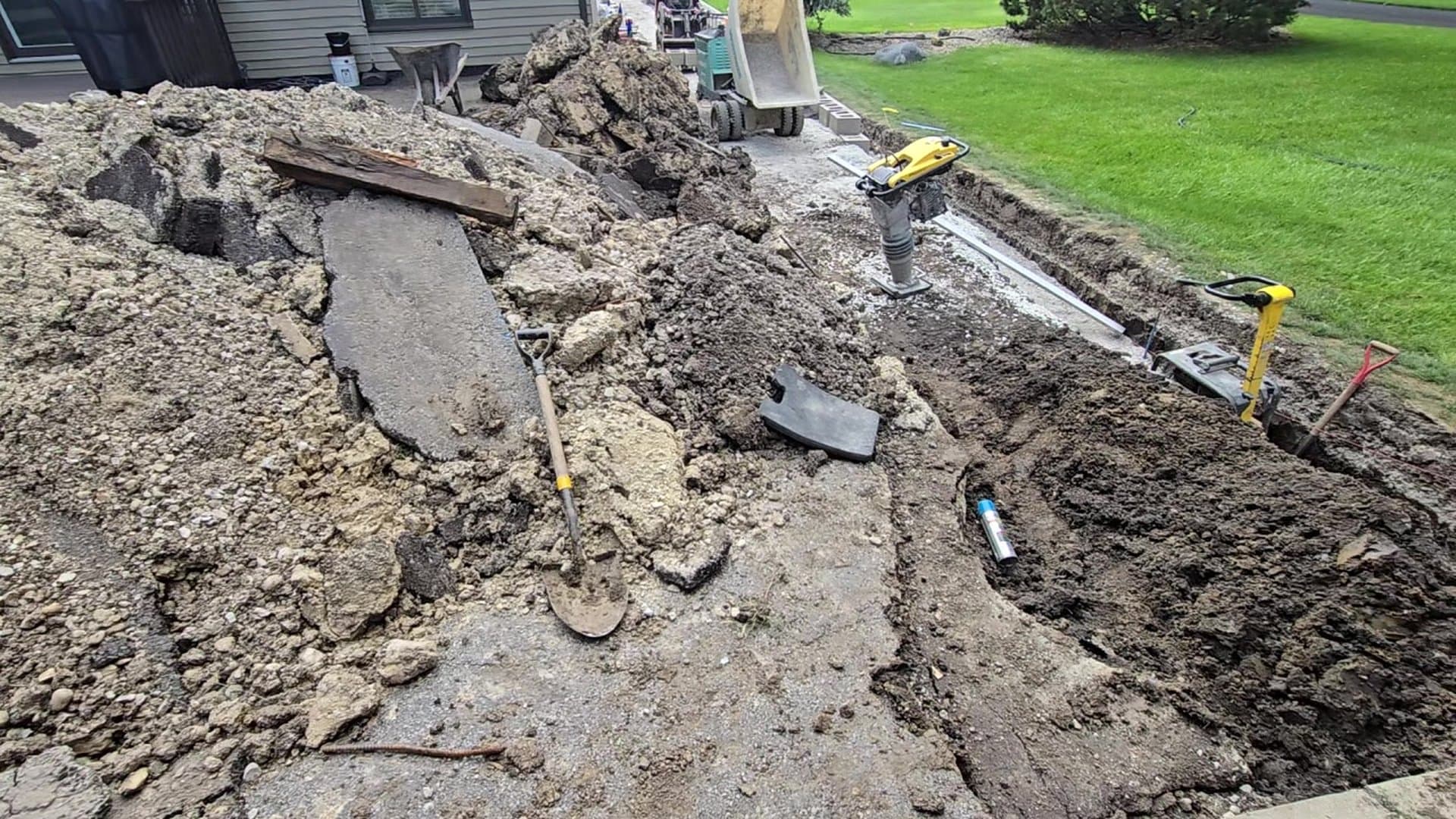 Una excavación de zanja abierta en una propiedad residencial, con equipo de compactación durante la instalación de servicios subterráneos.