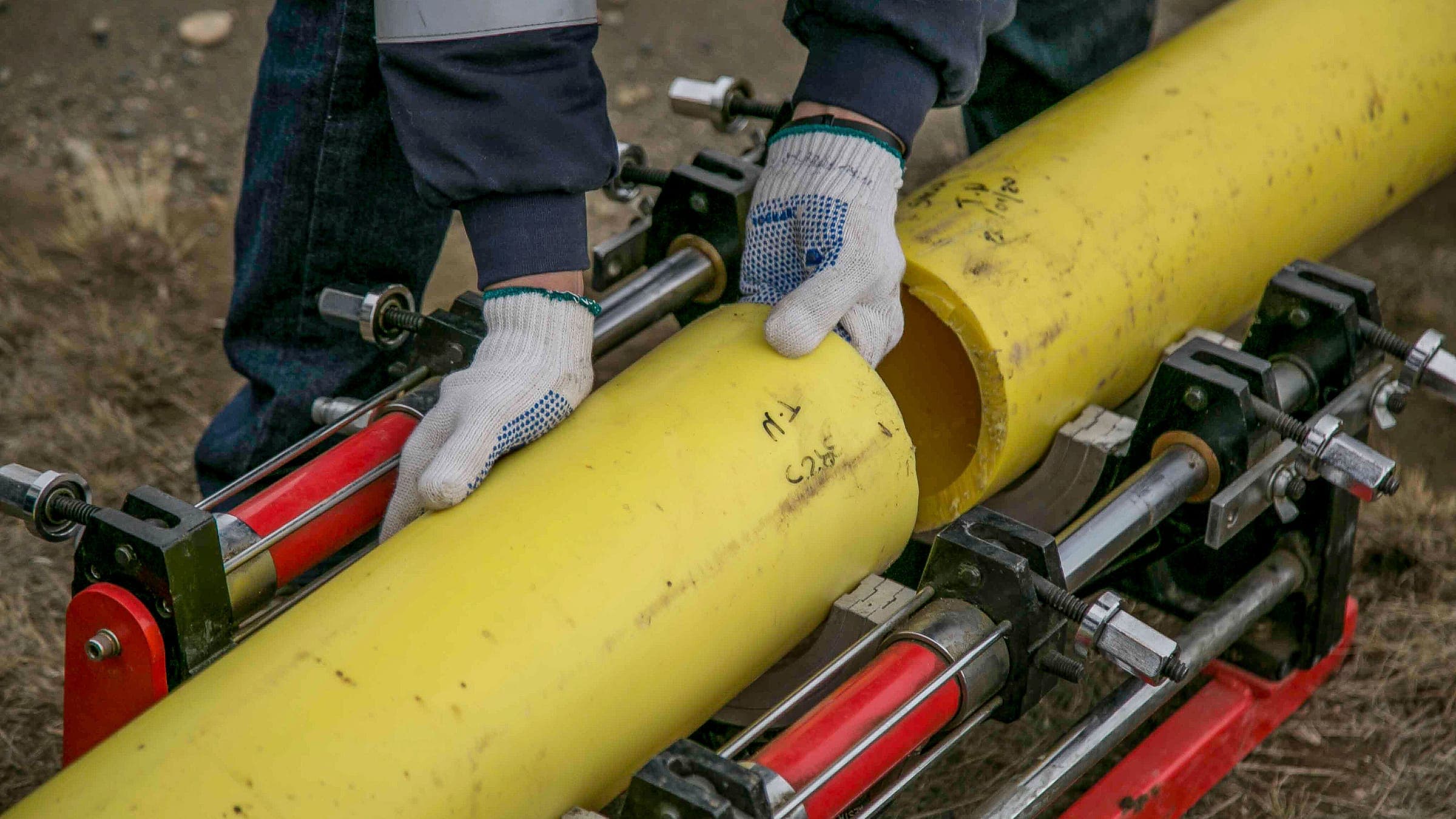 Un trabajador con guantes alineando un tramo de tubería de polietileno amarilla sujeta en una máquina hidráulica de fusión a tope para su unión.