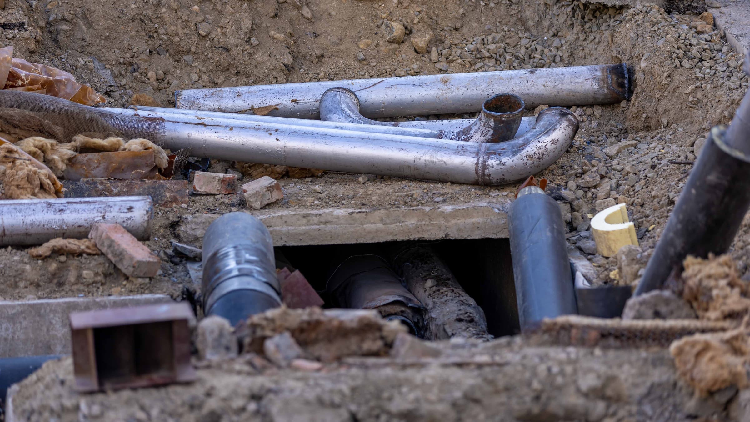Excavación abierta que expone tuberías y conexiones de servicios subterráneos durante un reemplazo de tubería.